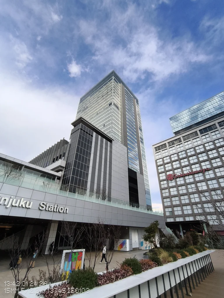 Nothing Phone (3a) Lite/超広角(15mm相当)、駅前の高層ビルを見上げ、ガラス壁面と雲模様の空が迫力ある構図で収まる、建物の稜線が鋭い