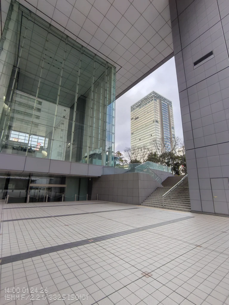 Nothing Phone (3a) Lite/超広角(15mm相当)、タイル張りの広場とガラス建築、階段の先に高層ビルが覗く無人の都市空間、幾何学的な陰影