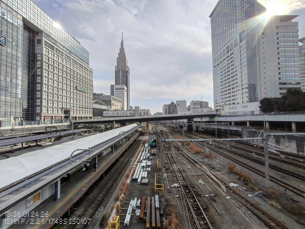 Nothing Phone (3a) Lite/超広角(15mm相当)、駅のホームと多数の線路が奥へ伸び、高層ビル群と雲が広がる俯瞰の都市景、線路の分岐が密集