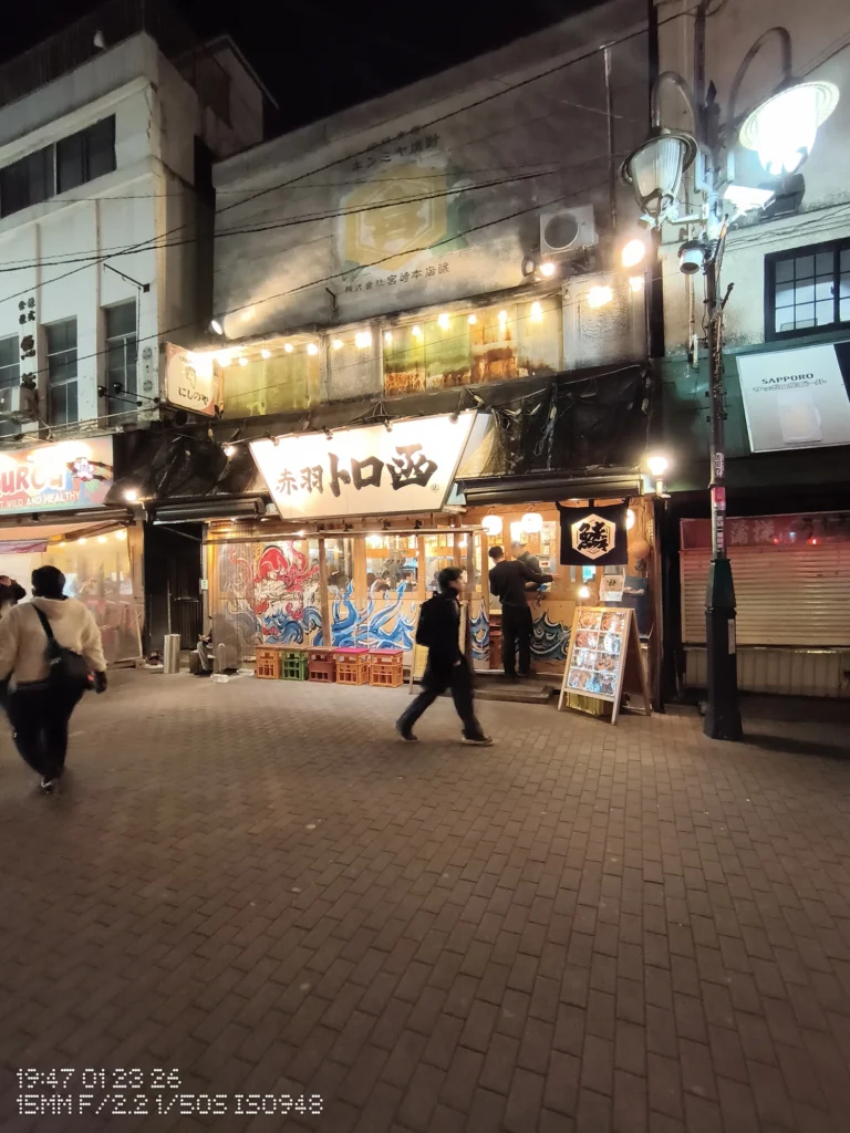 Nothing Phone (3a) Lite/カメラ:超広角/焦点距離:15mm相当/内容:夜の飲食店街の外観と大きな看板、街灯のにじみと歩道を行き交う人が写る夜景