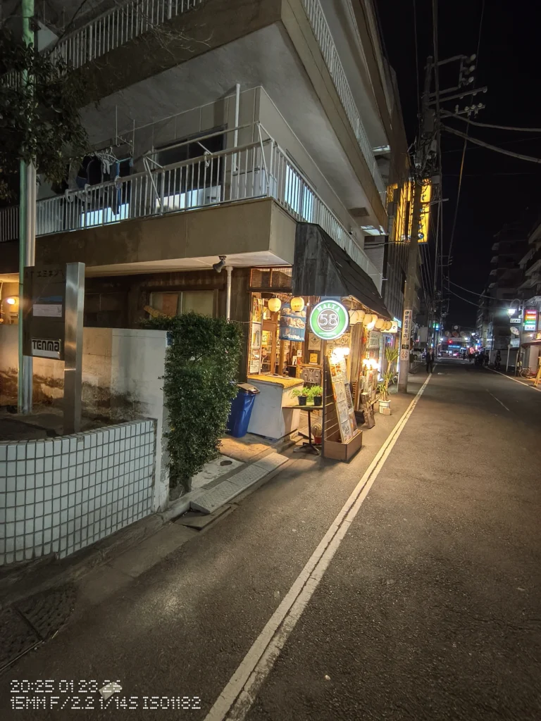 Nothing Phone (3a) Lite/カメラ:超広角/焦点距離:15mm相当/内容:夜の通り沿いに小さな飲食店の看板が灯り、電線と街灯が奥へ続く静かな夜景