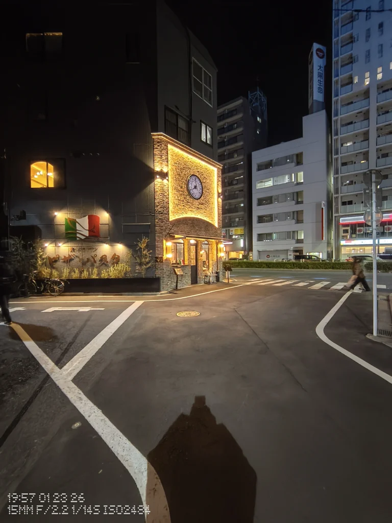 Nothing Phone (3a) Lite/カメラ:超広角/焦点距離:15mm相当/内容:夜の交差点に時計のある建物が暖色で照らされ、横断歩道と街灯の光が広がる夜景
