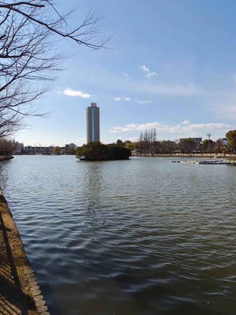 広大な池を囲む公園の風景。水面の波紋と、中央に浮かぶ島、背景の青空が織りなす開放感。Redmi Note 15 Pro 5G(2億画素モード)で撮影。
