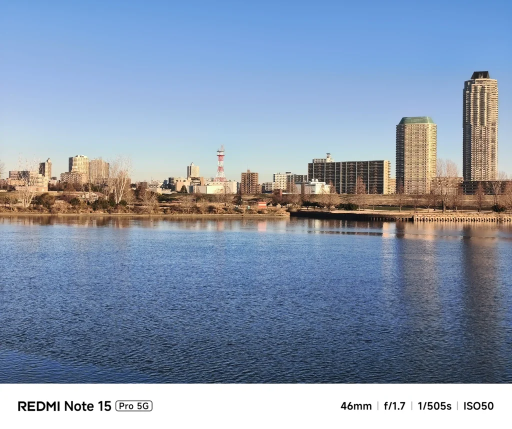 川越しに望む都市のスカイライン。青い水面と立ち並ぶタワーマンション群。Redmi Note 15 Pro 5Gで撮影。