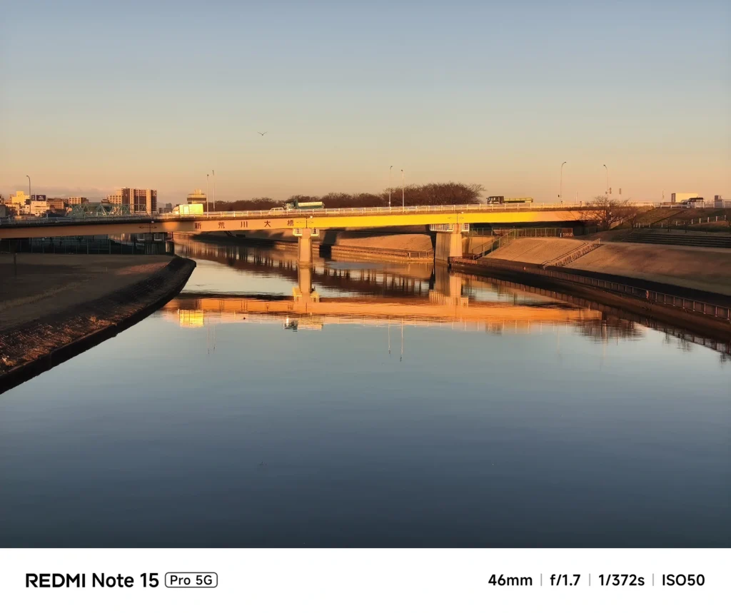 夕日に照らされ黄金色に輝く新荒川大橋と、鏡のように静かな川面への映り込み。Redmi Note 15 Pro 5Gで撮影。