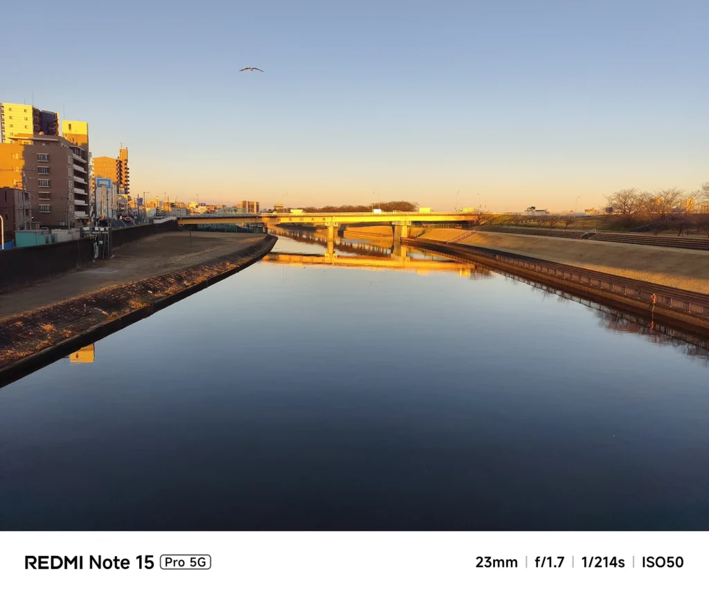 Redmi Note 15 Pro 5G 実機レビュー。夕暮れ時の新芝川と橋を捉えた風景。23mm f/1.7による夕日の諧調と水面の反射を検証。