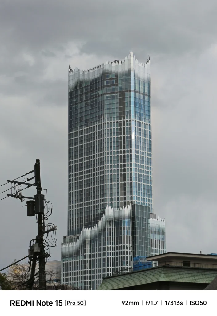 曇り空にそびえ立つ、装飾的な外壁が特徴的な高層ビルのクローズアップ。Redmi Note 15 Pro 5G(92mm)で撮影。