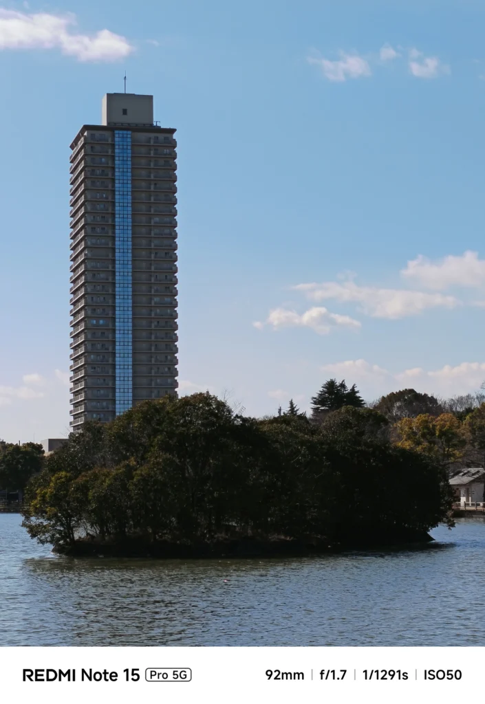 公園の池の島と、背景に立つ高層マンション。ズームによる圧縮効果を活かした風景。Redmi Note 15 Pro 5G(92mm)で撮影。