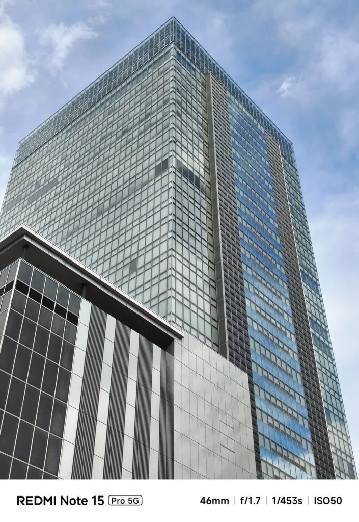 高層ビルの上部を捉えた標準域の構図。空の青さとガラス外装の反射。Redmi Note 15 Pro 5G(46mm/2倍)で撮影。