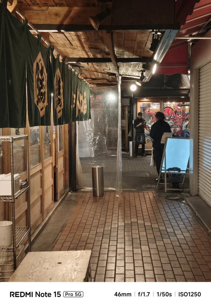 閉店後の商店街の路地。ビニールカーテン越しに漏れる光と静かな夜の空気感。Redmi Note 15 Pro 5G(46mm/夜景モード)で撮影。