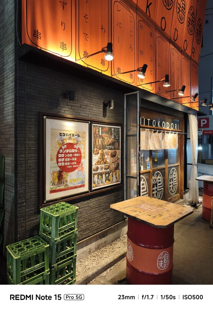 ドラム缶テーブルが並ぶ立ち飲み店「いっとく鳥」の店先。夜の活気を感じさせるスナップ。Redmi Note 15 Pro 5G(23mm/夜景モード)で撮影。