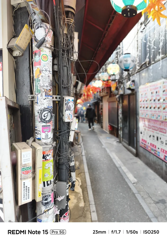 新宿「思い出横丁」の電柱に貼られた無数のステッカー。背景をぼかして質感を強調。Redmi Note 15 Pro 5G(ポートレートモード)で撮影。