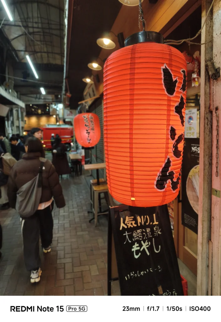 商店街の入り口に吊るされた巨大な赤い赤提灯。活気ある街並みを背景にしたスナップ。Redmi Note 15 Pro 5G(ポートレートモード)で撮影。