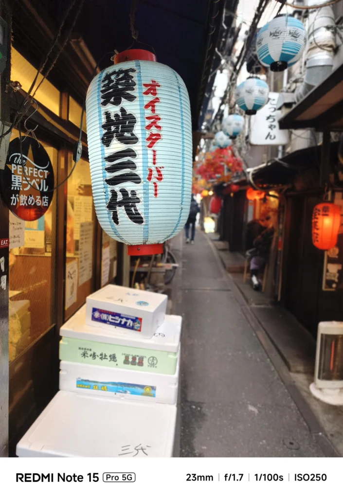 居酒屋の軒先に吊るされた「築地三代」の提灯。路地の奥行きを感じさせるボケ味。Redmi Note 15 Pro 5G(ポートレートモード)で撮影。