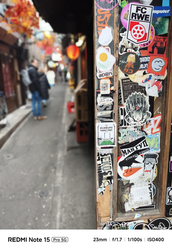 路地の入り口の柱に重なり合うステッカーやグラフィティ。被写界深度の浅い描写。Redmi Note 15 Pro 5G(ポートレートモード)で撮影。
