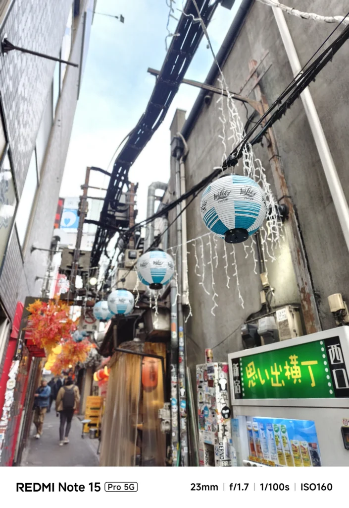 頭上に連なる水色の提灯と、複雑に入り組んだ電線が作る路地裏の風景。Redmi Note 15 Pro 5G(ポートレートモード)で撮影。
