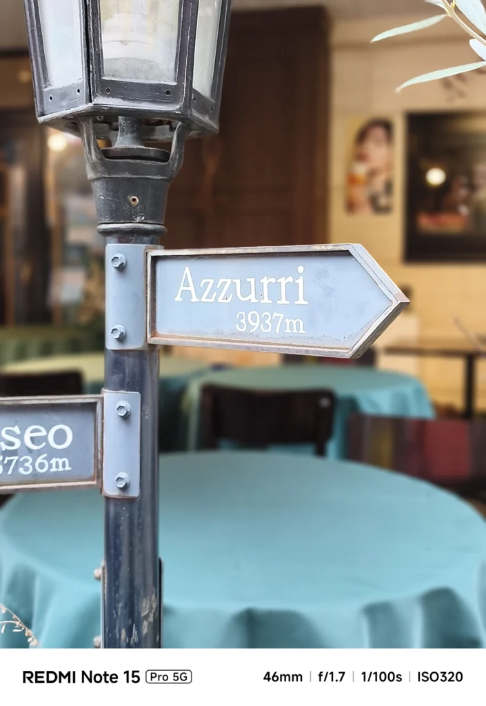 「Azzurri 3937m」と書かれた案内標識のクローズアップ。背景のテラス席を滑らかに処理。Redmi Note 15 Pro 5G(ポートレートモード)で撮影。