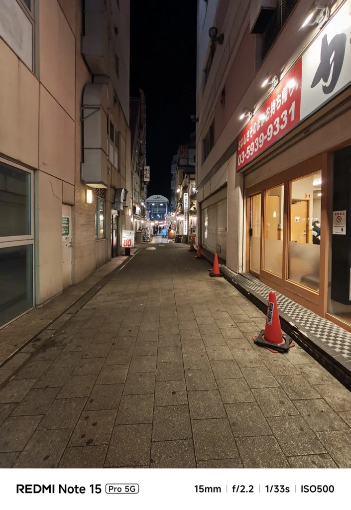 夜の静かな裏路地のパースペクティブ。建物の壁面と遠くの明かりが作る都会の夜景。Redmi Note 15 Pro 5G(15mm/夜景モード)で撮影。