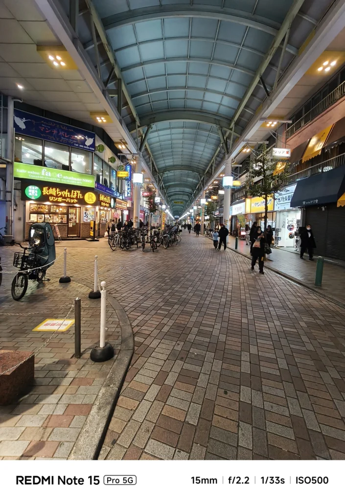 アーケード商店街(ララガーデン等)のパノラマビュー。高い天井と並ぶ店舗の照明。Redmi Note 15 Pro 5G(15mm/夜景モード)で撮影。