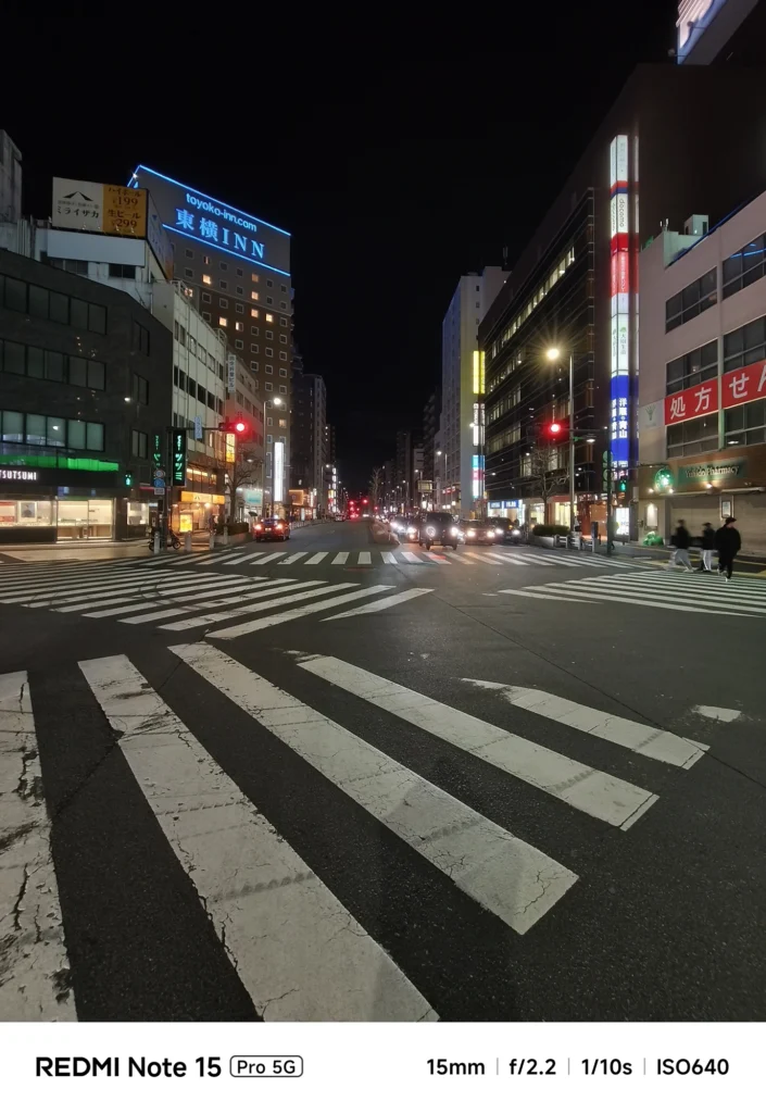 夜の幹線道路の交差点。横断歩道のラインと周囲のビル、車の光跡。Redmi Note 15 Pro 5G(15mm/夜景モード)で撮影。