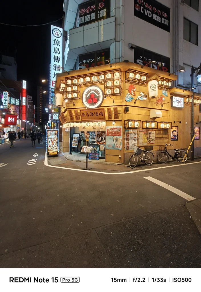 夜の角地に立つ賑やかな外観の「魚鳥傳酒場」。提灯の灯りと超広角によるダイナミックな描写。Redmi Note 15 Pro 5G(15mm/夜景モード)で撮影。