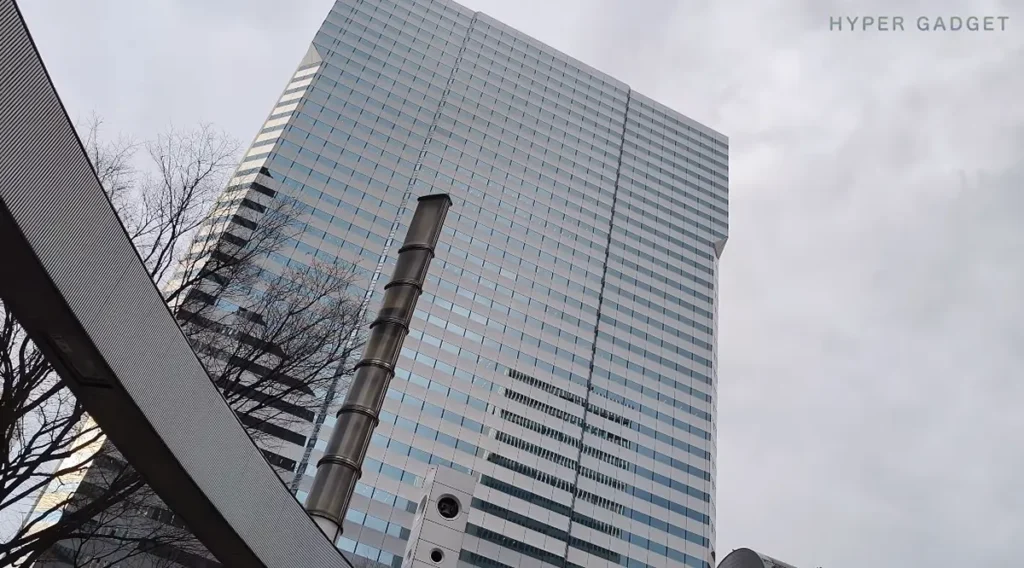 曇り空の下で見上げる高層ビルと煙突のローアングル動画サムネイル。Redmi Note 15 Pro 5Gで撮影。