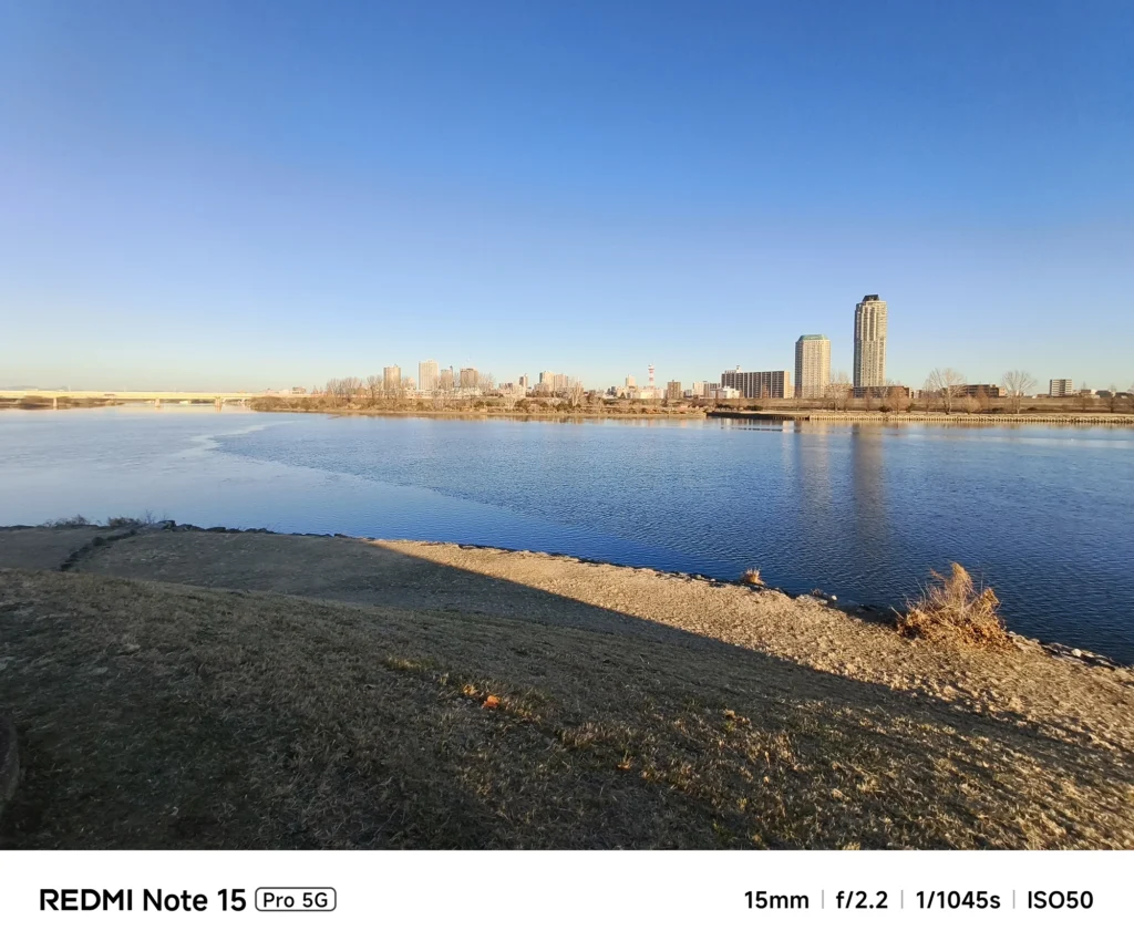 Redmi Note 15 Pro 5G 超広角15mm作例。夕暮れの荒川河川敷から望む川口方面の高層ビル群と穏やかな川面の描写。