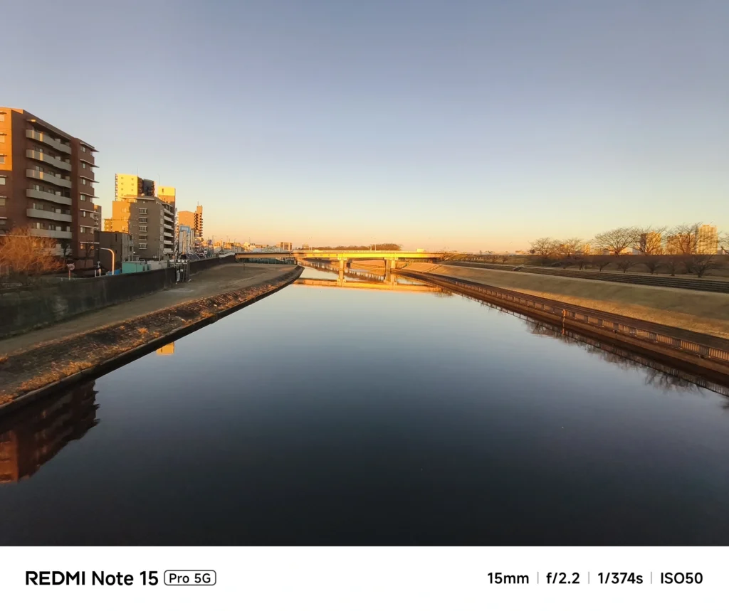 Redmi Note 15 Pro 5G 超広角15mmで撮影した夕方の新芝川。夕日に照らされる護岸のビル群と静かな水面の対比。