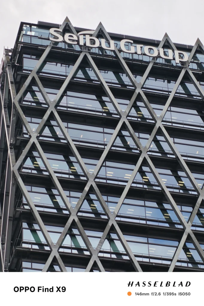 端末名：Find X9／カメラ：望遠／焦点距離：146mm相当／内容：Seibu Groupの看板がある高層ビル上部を望遠で引き寄せ、圧縮効果で格子外装と窓面を強調した日中の建築描写