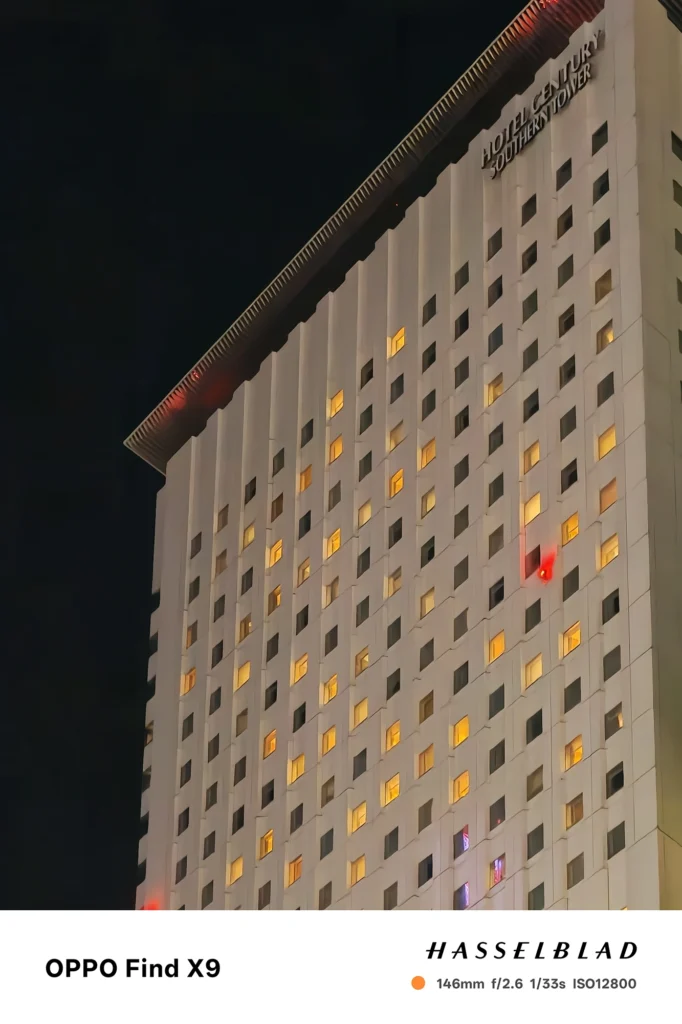 端末名：Find X9／カメラ：望遠／焦点距離：146mm相当／内容：白い外壁に小窓の灯りが点在する建物を望遠で圧縮し、点光源の規則性が夜景の静けさと高さを際立てる