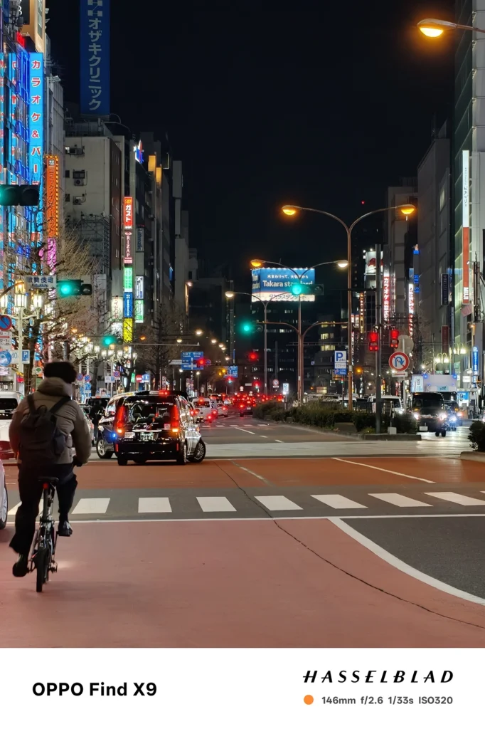 Find X9／カメラ：望遠／焦点距離：146mm相当／内容：ネオン看板と信号、車の灯りが続く大通りを望遠で圧縮し、光源の密度と都市の奥行きが強調される夜景描写
