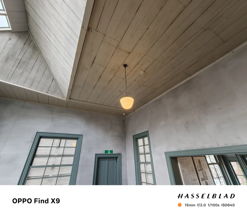 端末名：Find X9／カメラ：超広角／焦点距離：15mm相当／内容：木の天井と吊り照明、窓枠のある室内を見上げ気味に広角撮影し、板目と陰影の階調が分かる昼間の室内