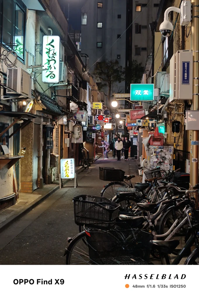 端末名：Find X9／カメラ：メイン（広角）2倍ズーム／焦点距離：48mm相当／内容：提灯や小さな看板が並ぶ飲食店街の路地を2倍ズームで引き寄せ、点光源の連なりと奥行きが強調された夜景