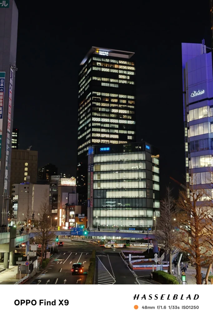 端末名：Find X9／カメラ：メイン（広角）2倍ズーム／焦点距離：48mm相当／内容：交差点周辺のビル群を2倍ズームで引き寄せ、窓明かりの点光源と暗い空のコントラストが強い都市夜景