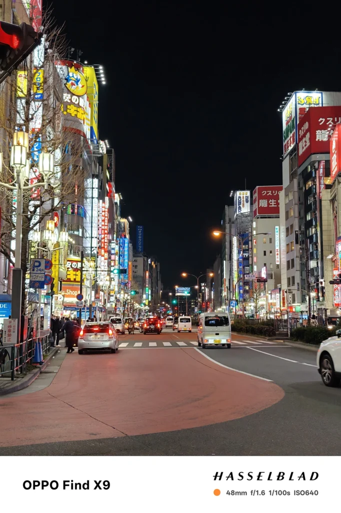 端末名：Find X9／カメラ：メイン（広角）2倍ズーム／焦点距離：48mm相当／内容：ROCKETの看板が下がる細い路地を2倍ズームで引き寄せ、壁面のステッカーや配管と奥の自転車が照明で浮かぶ夜景