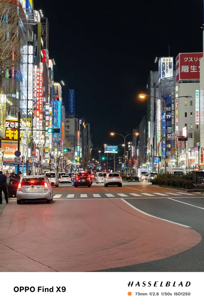 端末名：Find X9／カメラ：望遠／焦点距離：73mm相当／内容：大通りのビル看板と車灯を望遠で引き寄せ、信号や広告光の密度を圧縮効果で詰めて都市夜景のスケール感を表現