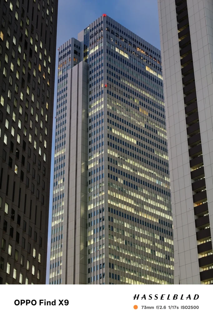 端末名：Find X9／カメラ：望遠／焦点距離：73mm相当／内容：ビルに挟まれた高層建築を望遠で圧縮し、薄暮の空と窓明かりの反復を引き寄せて立体感を出した夜景