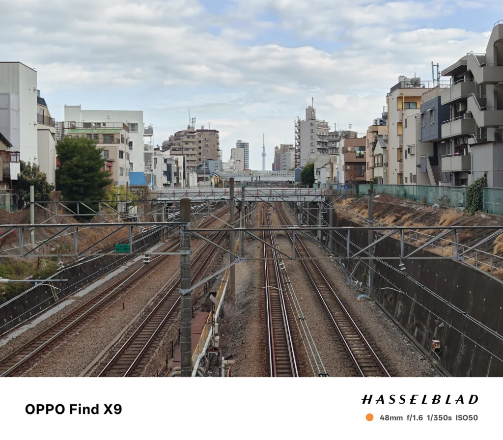 OPPO Find X9 メインカメラ2x（48mm）で撮影：線路が奥へ伸びる都市風景、遠景にスカイツリー