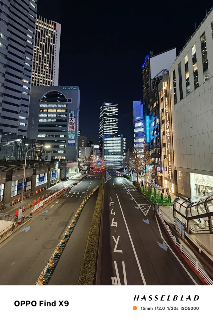 端末名：Find X9／カメラ：超広角／焦点距離：15mm相当／内容：歩道橋から見下ろす道路と高層建物を写し、街灯と窓明かりが奥へ続く夜の都市風景