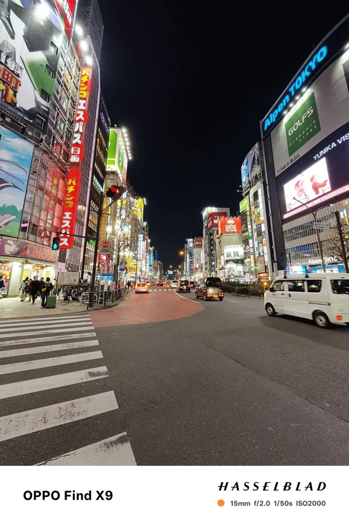 Find X9／カメラ：超広角／焦点距離：15mm相当／内容：看板とネオンが並ぶ繁華街の通りを広角で写し、車列と街灯の光が続く夜景