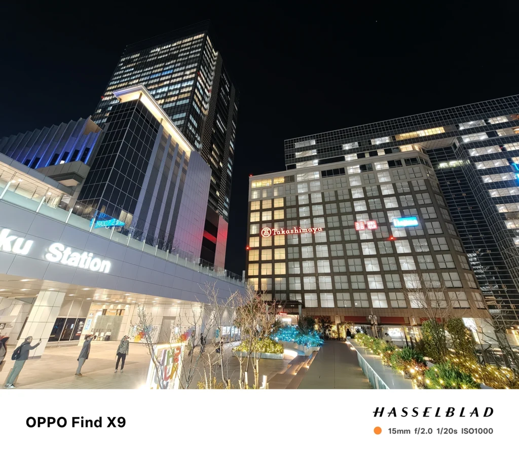 端末名：Find X9／カメラ：超広角／焦点距離：15mm相当／内容：駅前の広い歩道と高層建物を写し、イルミネーションと室内光が混在する夜景