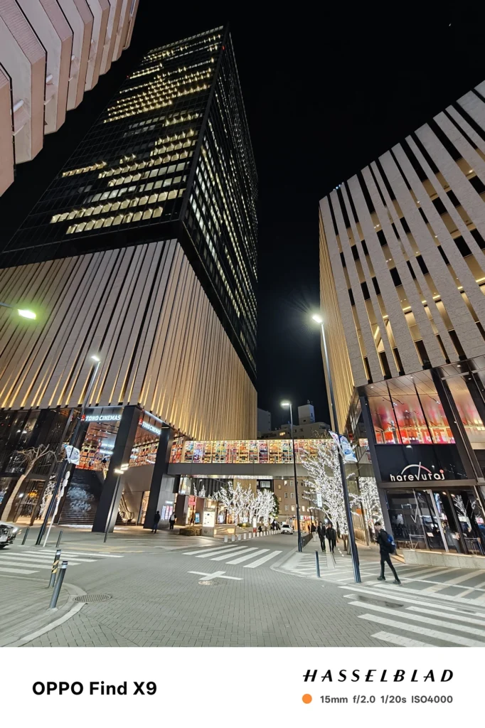 端末名：Find X9／カメラ：超広角／焦点距離：15mm相当／内容：高層ビルを見上げる広場の夜景で、街灯の光芒と建物の直線がくっきり出る構図