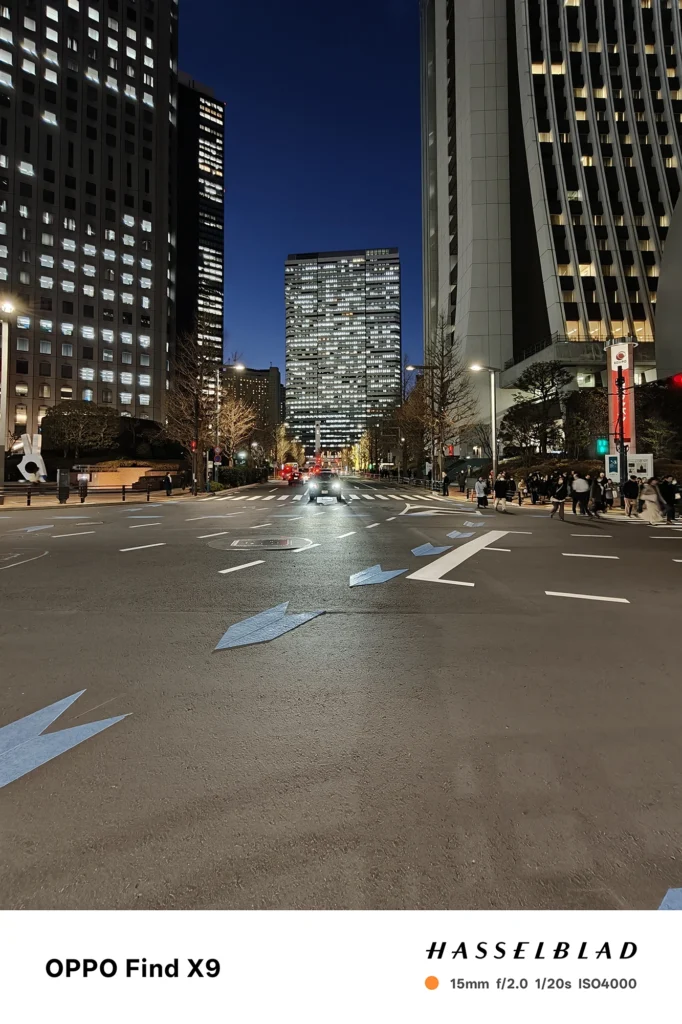 端末名：Find X9／カメラ：超広角／焦点距離：15mm相当／内容：高層ビルに囲まれた大通りを正面から捉え、車のライトと街灯が伸びる夜の都市風景