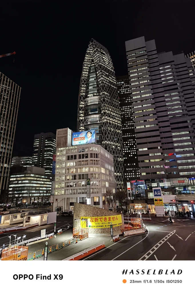 端末名：Find X9／カメラ：メイン（広角）／焦点距離：確認不能（mm相当）mm相当／内容：高層ビル群の夜景を見上げ、窓明かりの矩形パターンと街灯が暗い空にくっきり浮かぶ都会的な雰囲気