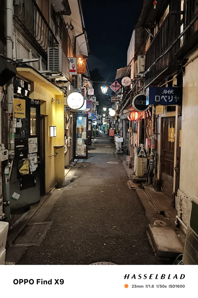 Find X9／カメラ：メイン（広角）／焦点距離：確認不能（mm相当）mm相当／内容：看板と提灯が密集する夜の細い路地を奥まで写し、街灯とネオンが店舗外観や自転車を照らす雑多な雰囲気