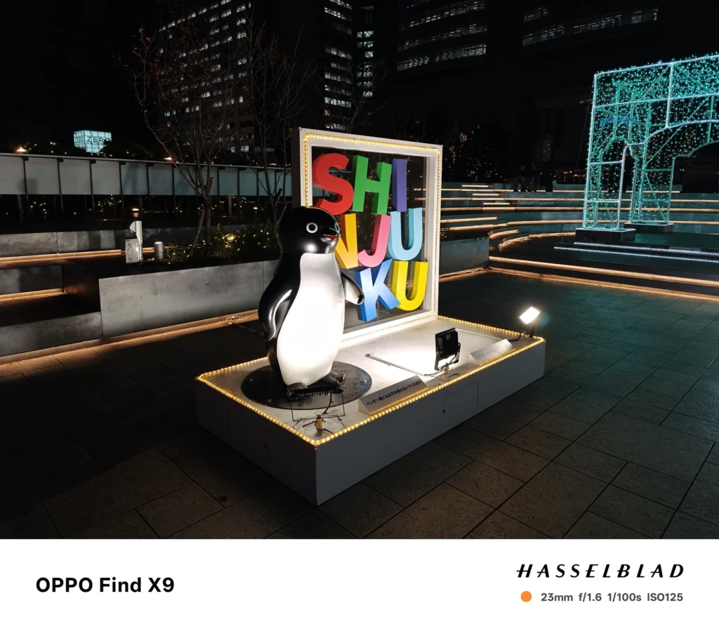 Find X9／カメラ：メイン（広角）／焦点距離：確認不能（mm相当）mm相当／内容：広場のイルミネーション展示を写し、カラフルなサインと白いオブジェがスポットライトで照らされる夜景の雰囲気