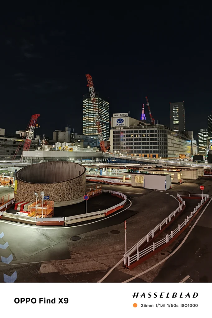 Find X9／カメラ：メイン（広角）／焦点距離：確認不能（mm相当）mm相当／内容：夜の工事エリアと高層ビルを俯瞰し、作業灯と窓明かりが道路のカーブを照らす都会夜景