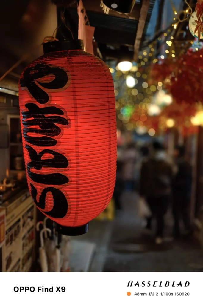 夜の路地で赤提灯を48mmポートレート撮影（OPPO Find X9）。背景の光を玉ボケにして被写体を強調。