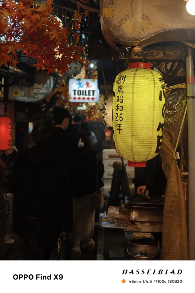 黄提灯と案内看板が並ぶ夜の路地を48mmポートレート撮影（OPPO Find X9）。発光のボケ表現を確認できる作例。