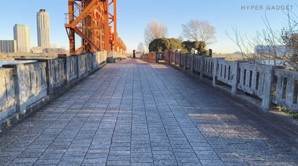 水門上の遊歩道を奥行き方向に撮影したショット(オレンジの鉄骨構造と冬の青空、Nothing Phone (3a) Lite動画作例)